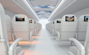 An image of an aircraft cabin, with white seats and seatback screens. A display on the ceiling shows clouds and blue sky inside the aircraft