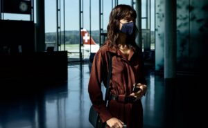 A women in an airport terminal with a mask on and a swiss aircraft in the background, IATA