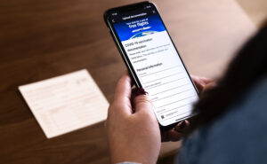 Woman holding a mobile device. The device is displaying a vaccine documentation verification form.