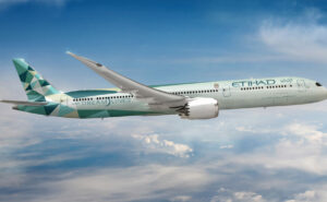 Greenliner Etihad Airways Boeing 787 Dreamliner aircraft in flight over white clouds and a blue sky.