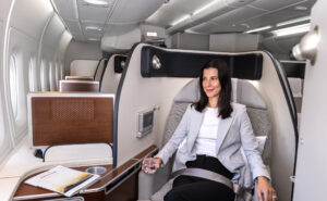 A female passenger is holding a drink, smiling, while sitting in Qantas' First Class seat.