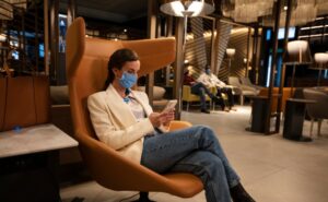 A women is sitting in a chair in the LATAM lounge. She is wearing a mask and using her mobile device.