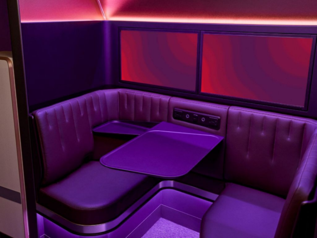 Virgin Atlantic's The Booth is pictured here with purple LED lights creating a modern, inviting atmosphere. The booth is comprised of two seats across from each other with a small table inbetween.