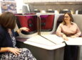Two women are sitting in business class seats on the AIX show floor.